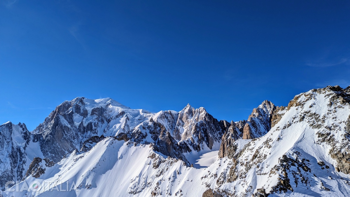 Spre stânga, acoperit de zăpadă, se vede vârful Mont Blanc (4808m).